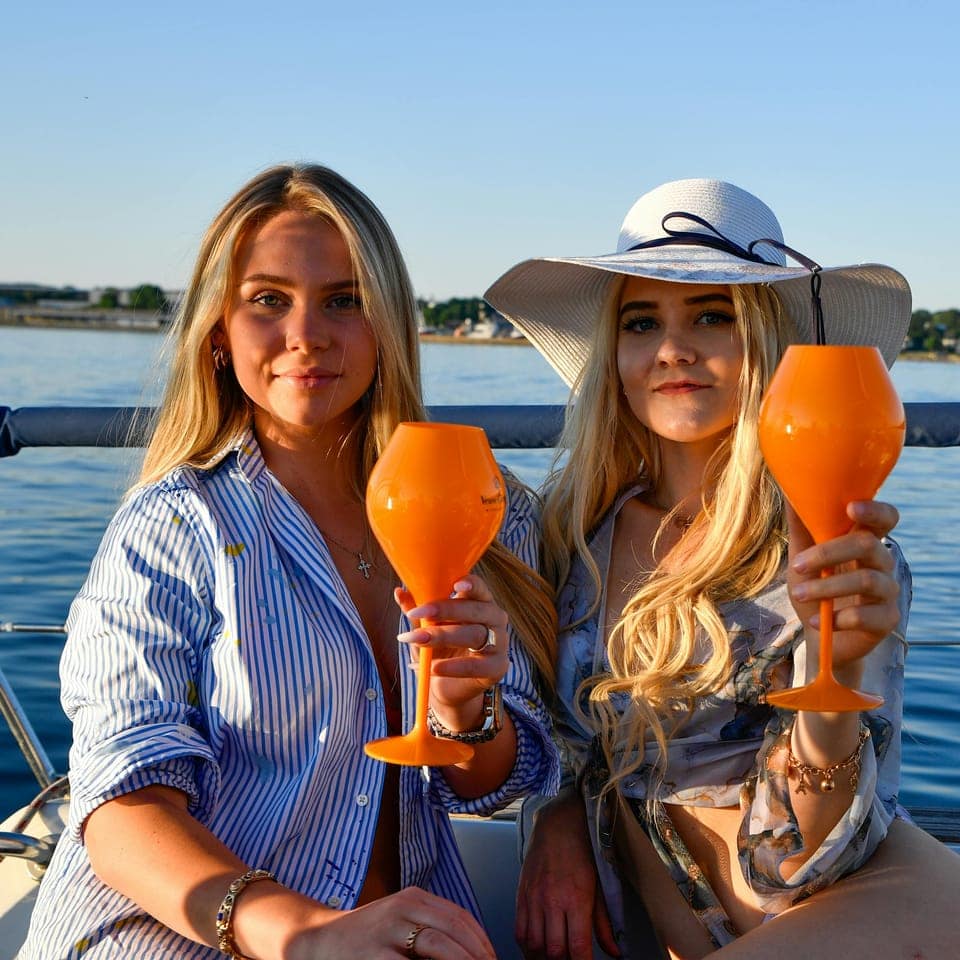 Två personer på en båt med orange champagneglas i solljus